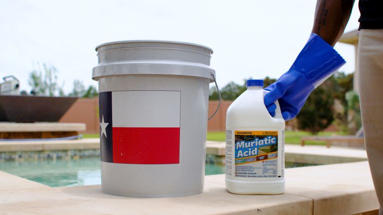 Champion Muriatic Acid Gloved Hand Gripping Jug Beside Flag Bucket